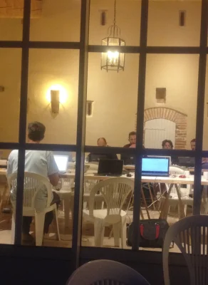 Ambiance nocturne, photo depuis l'extérieur d'un grand batiment, la nuit, où on voit à travers les portes fenêtres des personnes en train de coder