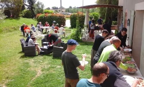 Ambiance pique nique, des personnes en train de se servir dans un buffet, d'autres en train de manger, dans un jardin