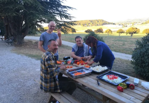 Ambiance collective, des personnes en train de nettoyer / couper des légumes, sur une table dans un jardin, pour le repas collectif 